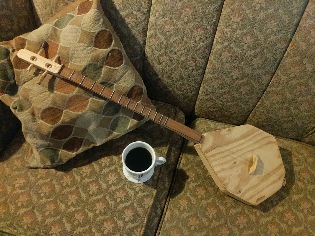 The finished dombra, displayed on a couch with a cup of coffee