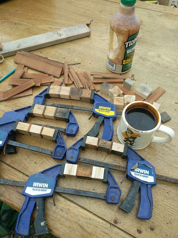 a pile of cut wooden pieces, some in clamps, and a cuppa coffee