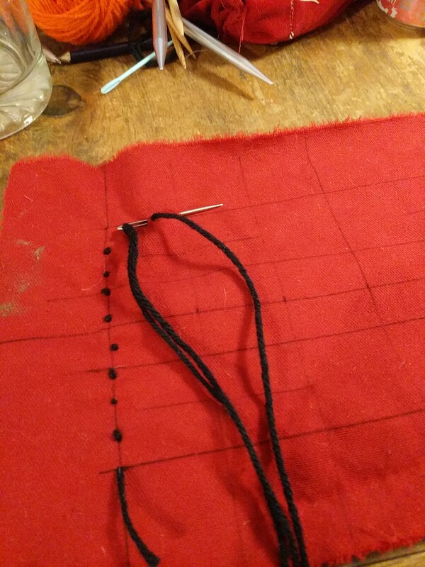 black yarn in a sewing needle, and a few stitches