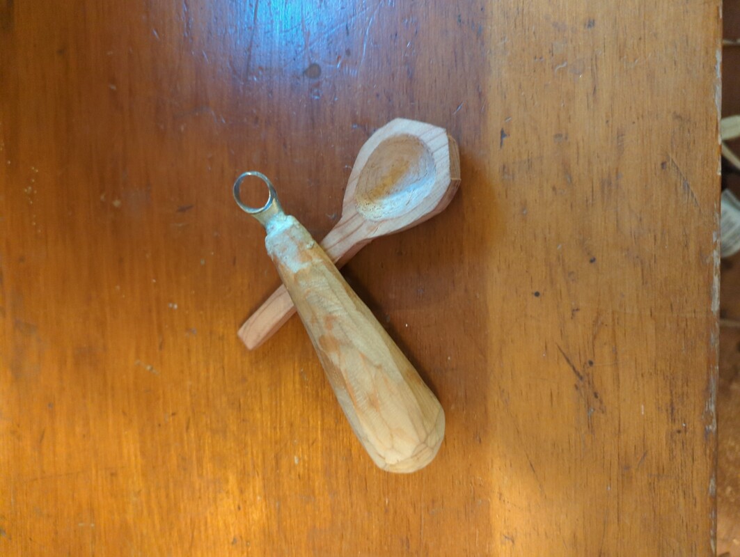 the scorp knife resting upon a wooden spoon. The handle and edge of the spoon is very rough, but the inside of the spoon is nicely carved 