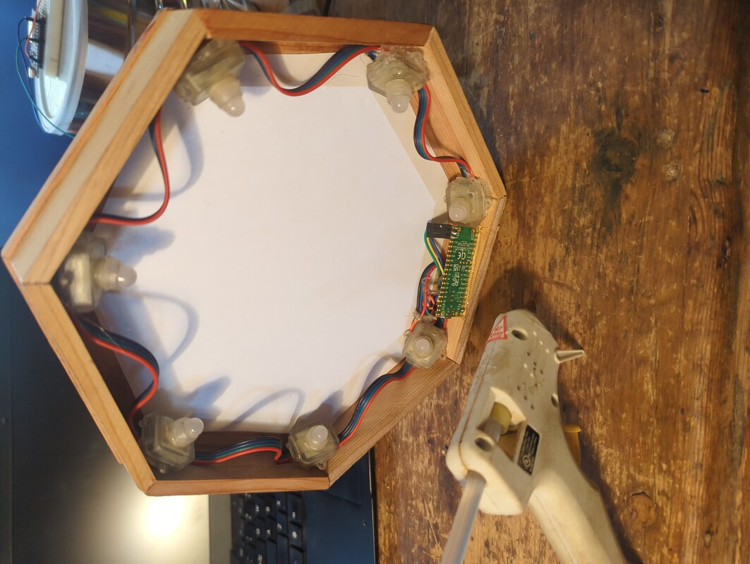 backside of the seven sided frame. there are seven pixel leds and a microcontroller hot glued to the inside of the frame