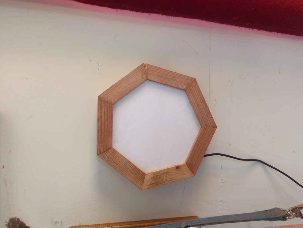 seven sided wooden fram hanging on a wall. there is a USB cable extending from the bottom of the frame
